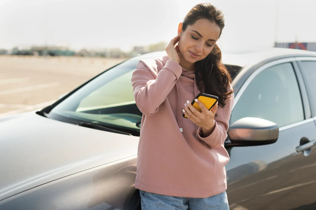 mujer recostada en el auto y mirando su telefono