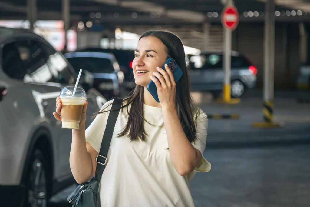 una mujer joven con cafe hablando por telefono en el estacionamiento (1)