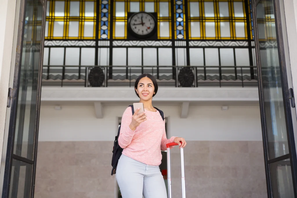 mujer sonriente que se coloca con la maleta en pasillo de la estacion